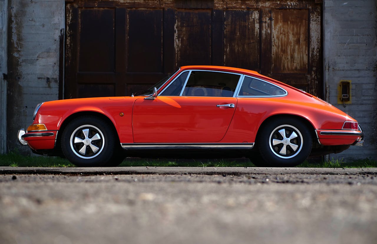 Vintage orange car side view parked against rustic urban backdrop, highlighting sleek design.
